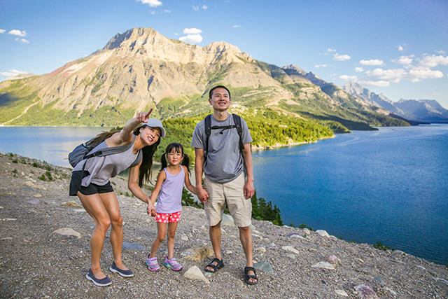 A young family is walking on the Prince of Wales hill, at Waterton Lakes National Park are looking up and pointing to the sky.