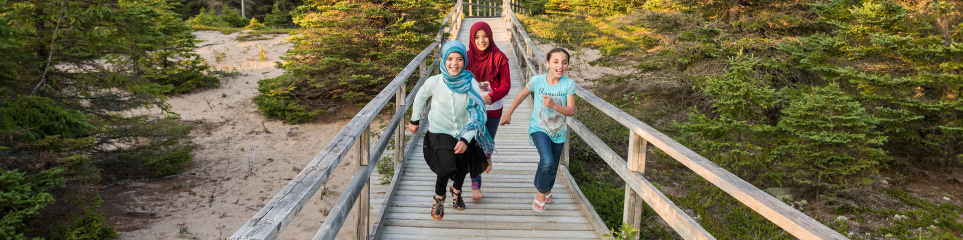 A group of children are running on a boardwalk with trees around them at Pukaskwa National Park.