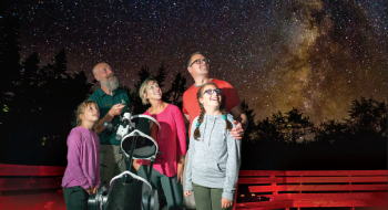 Une famille regarde une réserve de ciel étoilé à l'aide d'un télescope à côté d'un guide de Parcs Canada au cercle céleste au parc national et lieu historique national Kejimkujik.
