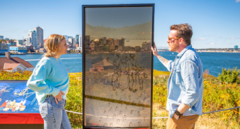 Des personnes regardent le panneau d’interprétation « Les Acadiens » au lieu historique national de l'Île-Georges.