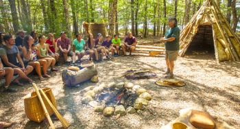 Group of tourists sit around a fire during an interpretation at Wejisqalia’ti’k at the Mi'kmaw encampment in Kejimkujik National Park and National Historic Site.