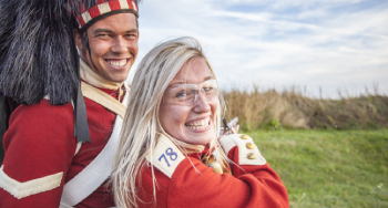 Une jeune femme se retourne tandis qu'elle se prépare à tirer à l'aide d'un fusil Snider-Enfield avec un interprète déguisé en soldat du 78e régiment des Highlanders, dans le cadre du programme « Prêt, visez, feu! » au lieu historique national de la Citadelle-d’Halifax.