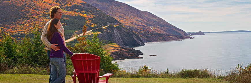 A couple admires the panoramic views of the Cabot Trail on Parks Canada red chairs