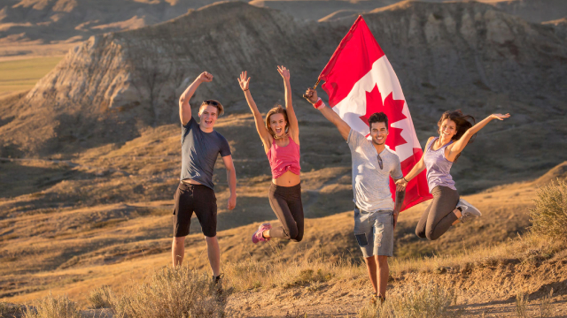 Un groupe de jeunes adultes célèbre le Canada à l'aide d'un drapeau canadien lors d'une randonnée sur le sentier de Butte-70-Mile du bloc Ouest, au parc national des Prairies.
