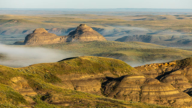 Fog runs through the rolling badlands of Grasslands National Park, striped, rocky hills.