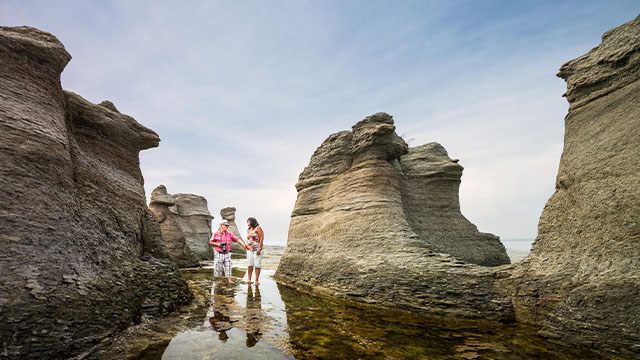 Two people exploring big monoliths in the Mingan Archipelago National Park Reserve.