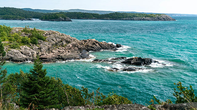 Rocky shorelines with trees surround stunning turquoise waters with waves in Pukaskwa national Park.