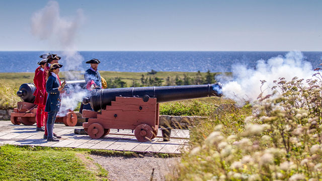 Two guides in period costume fire a cannon at Fortress of Louisbourg National Historic Site.