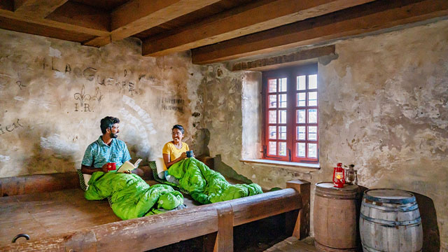 Two visitors in green sleeping bags smile at each other as they get ready to sleep in a prison at Fortress of Louisbourg National Historic Site.