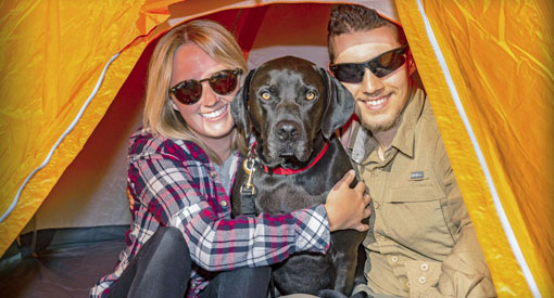 Un homme et une femme sont assis dans une tente et serrent un chien dans leurs bras.