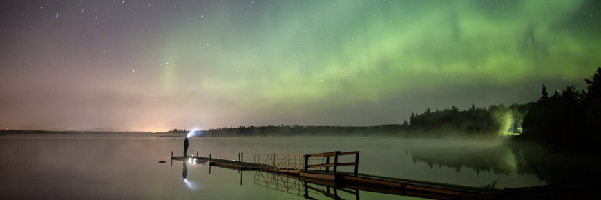 Visitor stands on a dock admiring the northern lights.