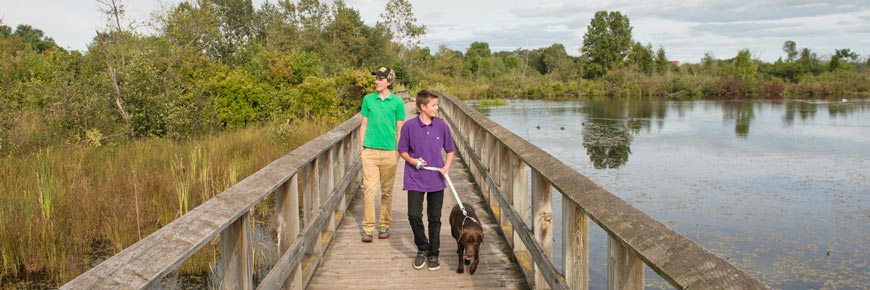 Deux visiteurs et leur chien marchant sur une promenade de bois dans un parc national. Le chien est en laisse.