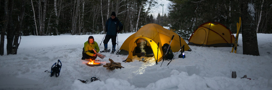 Des visiteurs en camping d’hiver près d’un feu de camp.
