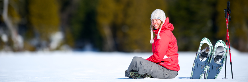 Une femme est assise sur la neige à côté de sa paire de raquettes au parc national de la Mauricie.