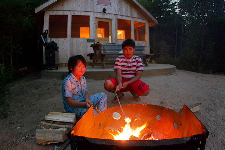 Deux enfants s'amusent à faire griller des guimauves devant leur chalet rustique sur l'île Beausoleil.