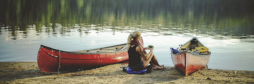 Une femme sirote son café à côté de canots au bord du lac Wapizagonke.
