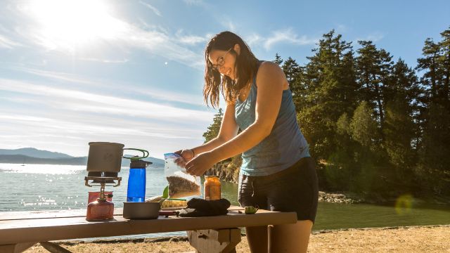 Under the summer sunshine, a visitor prepares food at a picnic table on the water's edge at Roesland in Gulf Islands.