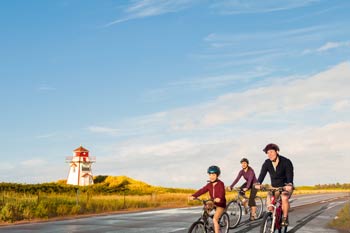 Three cyclists on a road near a lighthouse.