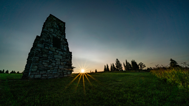 Sun setting on the horizon, casting warm light over grassy historic grounds at Fort St.Joseph National Historic Sites.