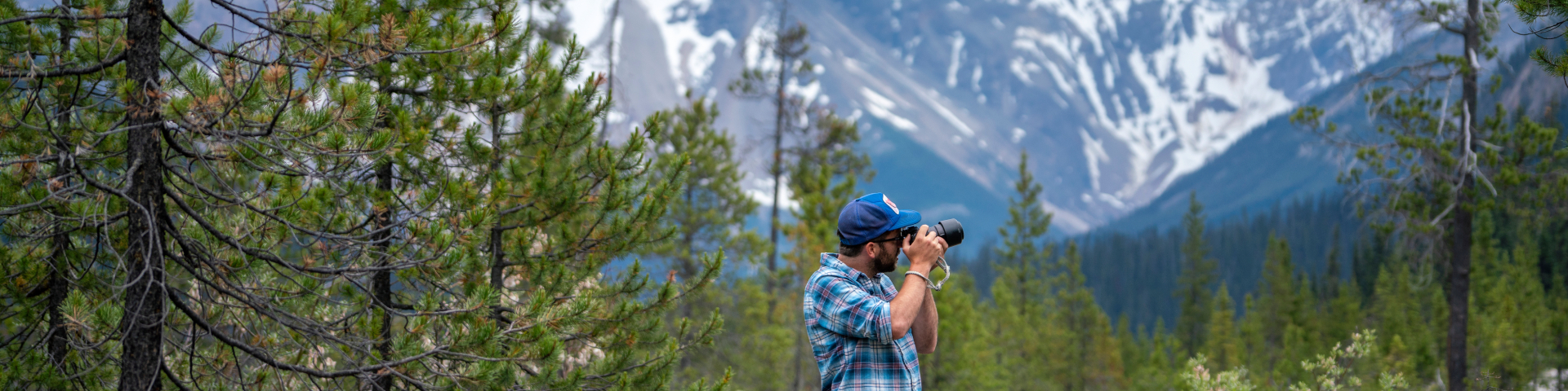 Visitor taking a photo in front of tall, rugged mountains under a clear sky.