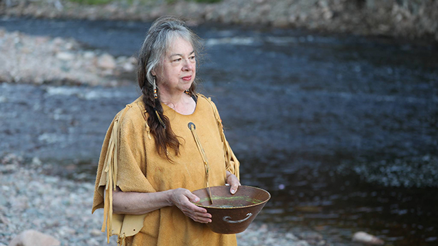 An Indigenous woman performing a ceremony with a bowl near the river