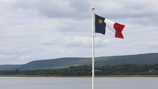 The acadian flag with coastal mountains in the background