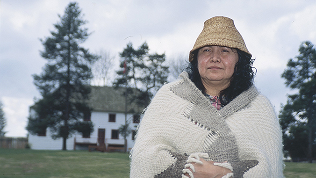 An Indigenous woman stands in front of Fort Langley