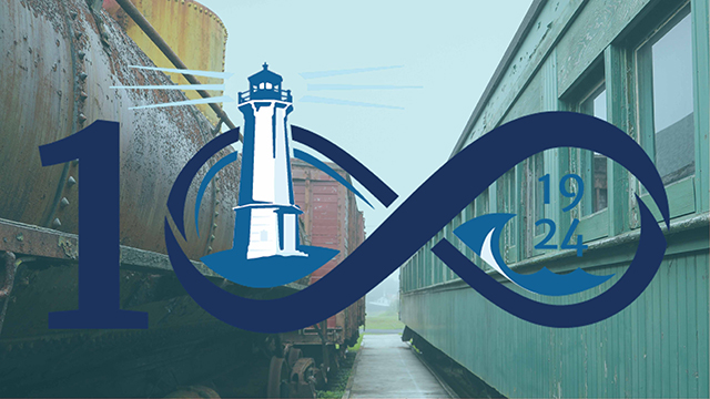 An outdoor walkway between the buildings of the Fortress of Louisbourg with a logo that has a 1 and the infinity symbol (number 100), a lighthouse, and the year 1924 in it