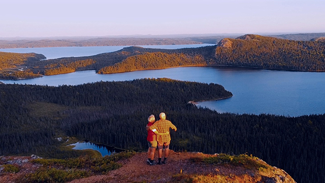 Two adults hug and admire the scenic view of the water and hills.