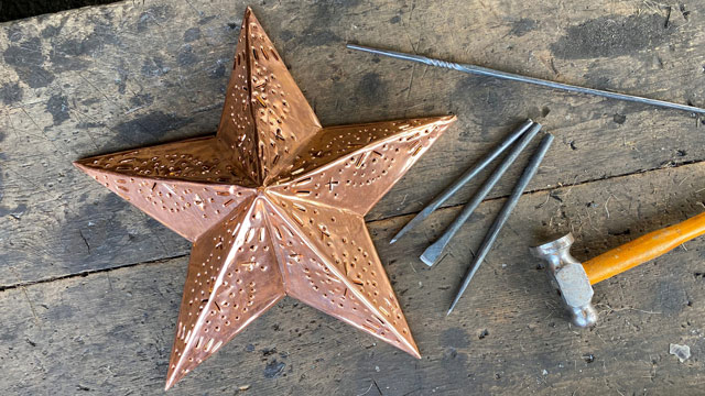 A copper star on a wooden table with 3 nails and a hammer.