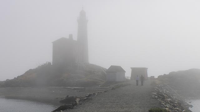 Two people walk toward the Fisgard Lighthouse on a foggy day.