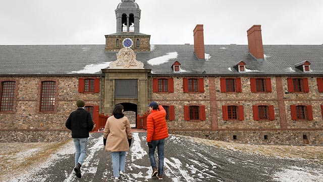 Three visitors head toward a building at the Fortress of Louisbourg National Historic Site in winter.