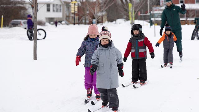 Two Parks Canada staff members and a group of children are cross-country skiing, buildings of the town of Chambly in the background.