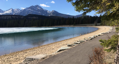 A paved trail runs along Lake Annette with mountains in the background.