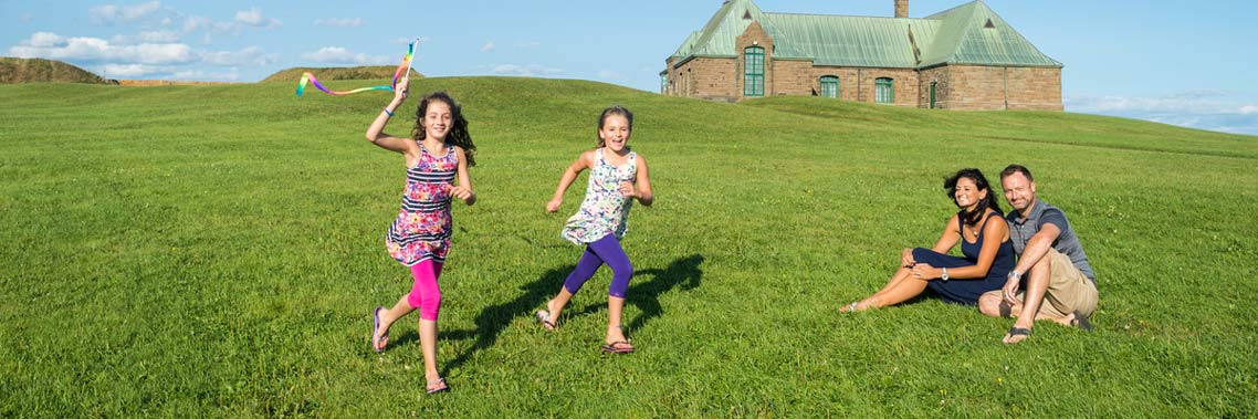 Deux jeunes filles, sous le regard de leurs parents, courent sur un vaste terrain gazonné.