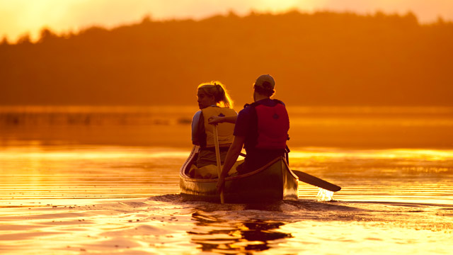 Two adults in a canoe during an orange sunset at Kejimkujik.
