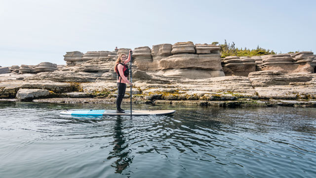 A young woman on a stand up paddle board near the shore of Petite Île au Marteau in Mingan Archipelago.