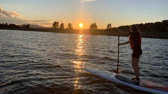 A visitor on a paddle board at sunset at Forillon National Park with Penouille Beach in the background.