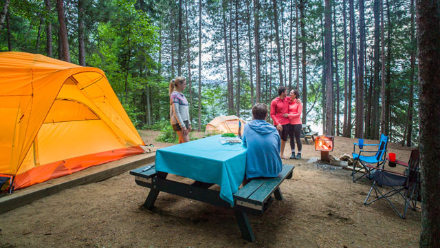 A Wapizagonke Lake canoe camping site with four visitors near a fire, a tent and a table in La Mauricie National Park.