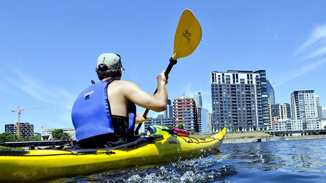 Two kayakers on Lachine Canal with buildings in the background.