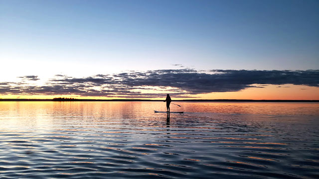 A visitor paddle boarding at sunset on Waskesiu Lake near King Island in Prince Albert.