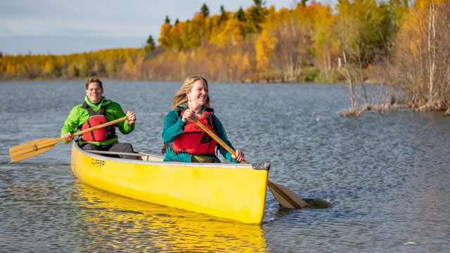 Two young adults paddle in a canoe during a sunny fall day on Astotin Lake in Elk Island.