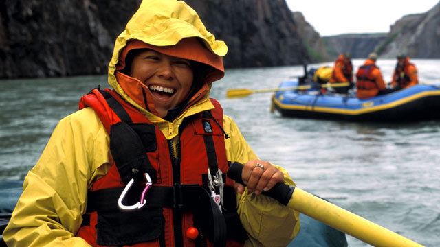 A close-up of an adult in a raft with a river, cliffs and another raft in the background in Ivvavik.