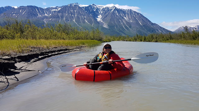 A woman in a packraft with mountains in the background in Kluane National Park and Reserve.
