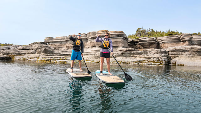 A couple paddle boarding in front of the  Petite Île au Marteau in Mingan Archipelago National Park Reserve.