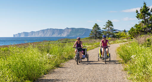 A family bikes on the Du Banc Trail along the ocean, with scenic cliffs in the background.
