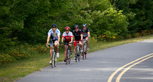 Four cyclists bike on the Parkway, green foliage in the background.