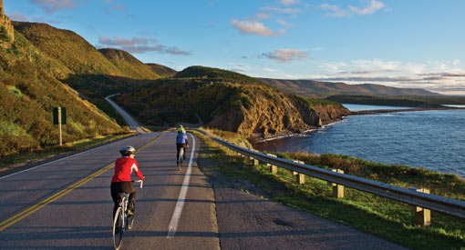 Two cyclists bike along the seaside on the Cabot Trail.