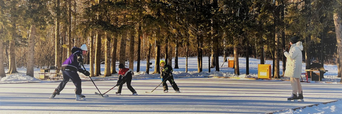 Four people play hockey on an outdoor rink in Riding Mountain National Park.