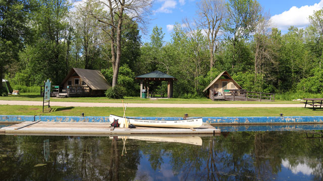 A canoe on a dock on the Rideau Canal with oTENTik tents in the background.